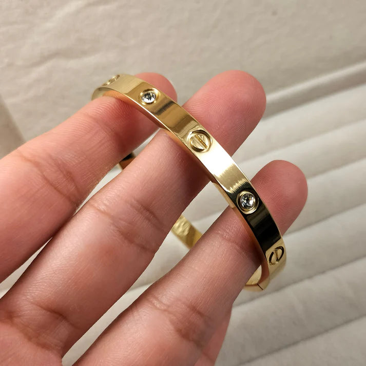 Gold Cartier bracelet by everray with three screws on a neutral background