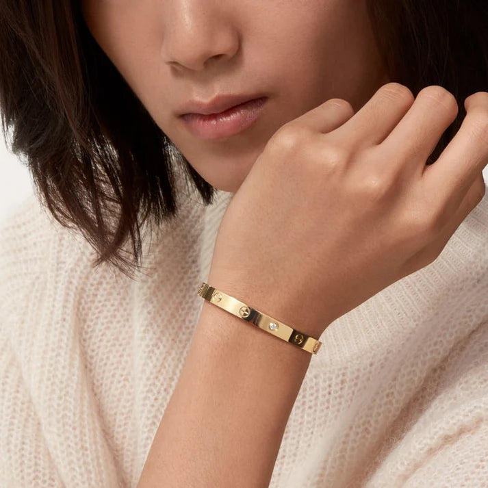 Close-up of a person wearing a gold bracelet on a neutral background