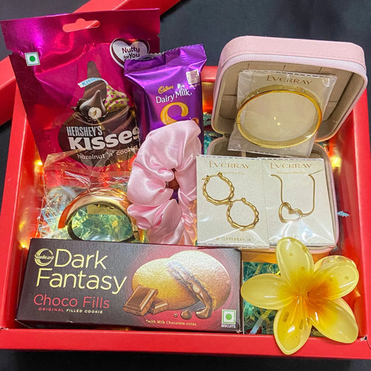 Gift box with chocolates, jewelry, and a flower on a dark background