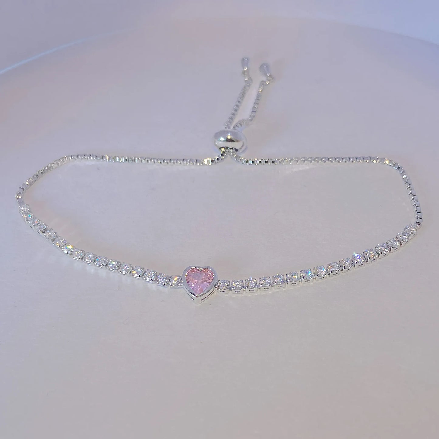 tesnnis bracelet with a heart-shaped pink gem on a white background