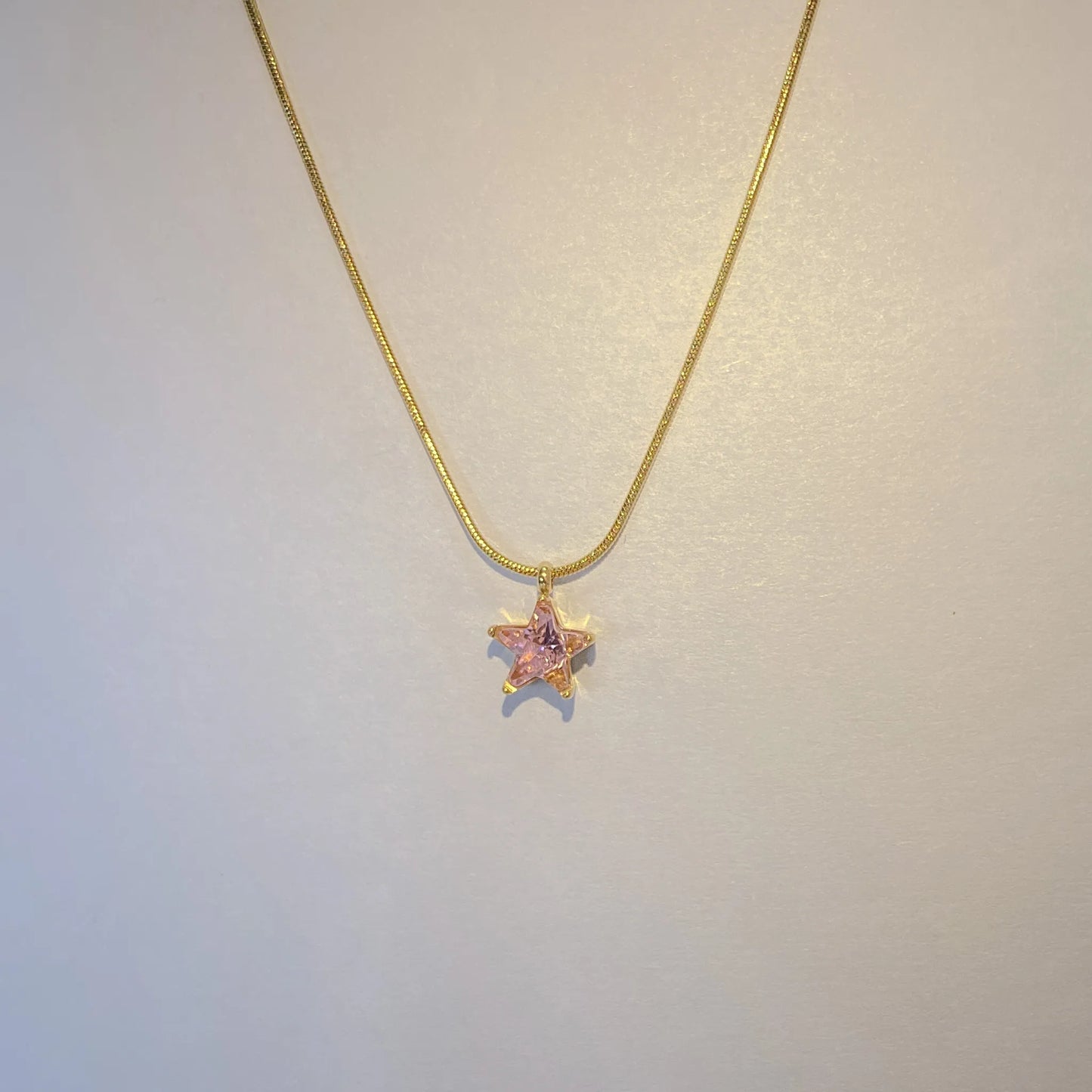 Gold necklace with a star-shaped pendant on a light gray background