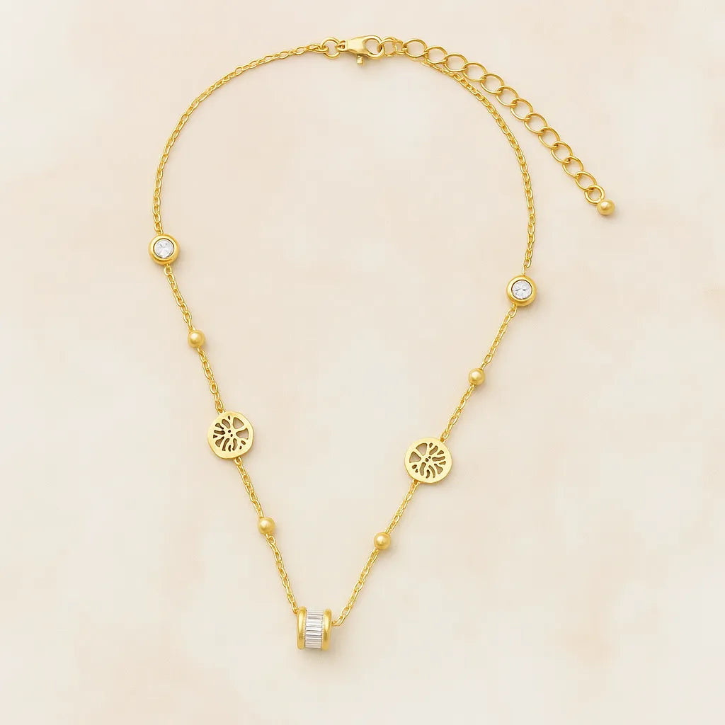 Gold-toned necklace featuring lotus-inspired medallions, bezel-set crystals, and a center baguette charm on adjustable chain.