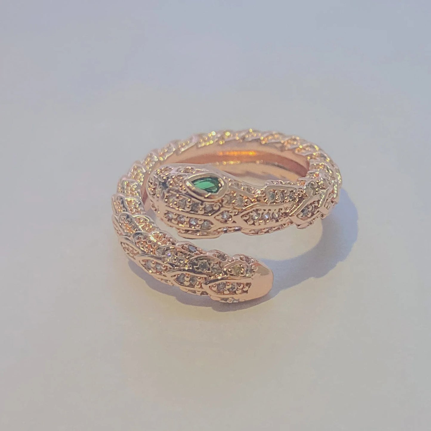 Rose gold snake-shaped ring with green gemstone on a light gray background
