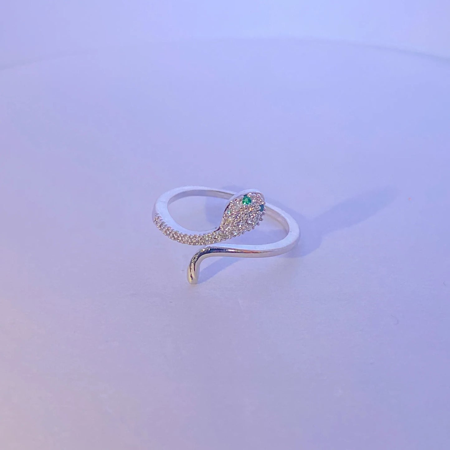 Silver snake-shaped ring with a green gemstone on a light purple background