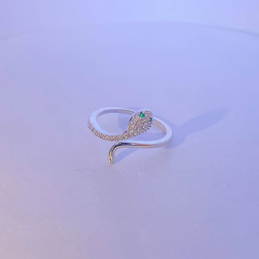 Silver snake-shaped ring with a green gemstone on a light purple background