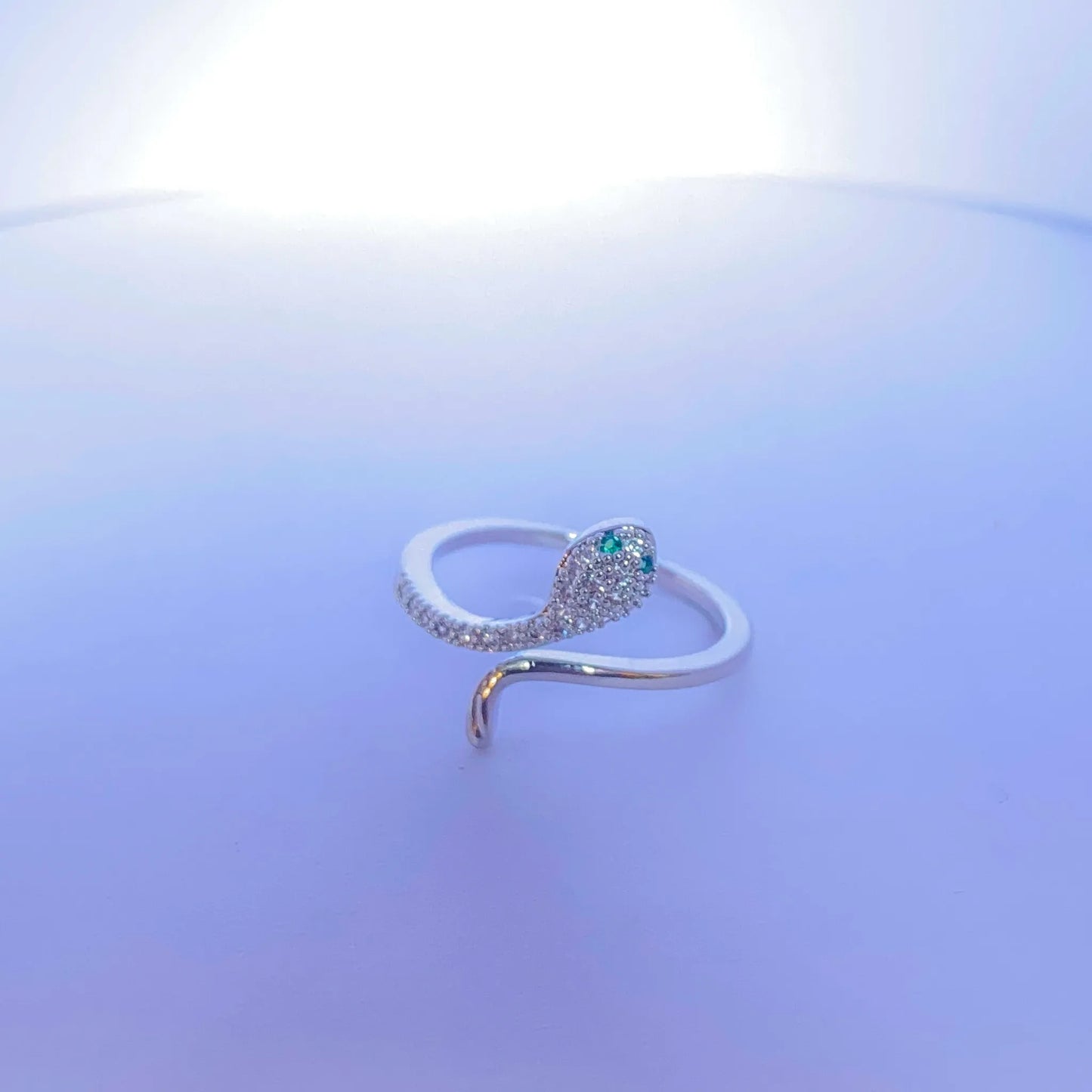 Silver snake-shaped ring with a blue gemstone on a light purple background