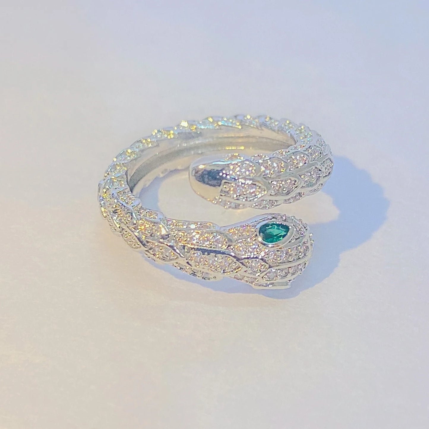 Silver snake-shaped ring with a green gemstone on a light gray background