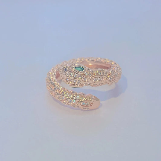 Rose gold snake-shaped ring with a green gemstone on a light blue background