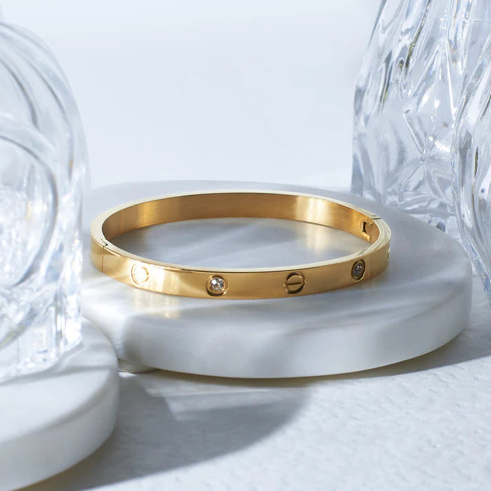 Gold bracelet with engraved symbols on a white surface with crystal vases.