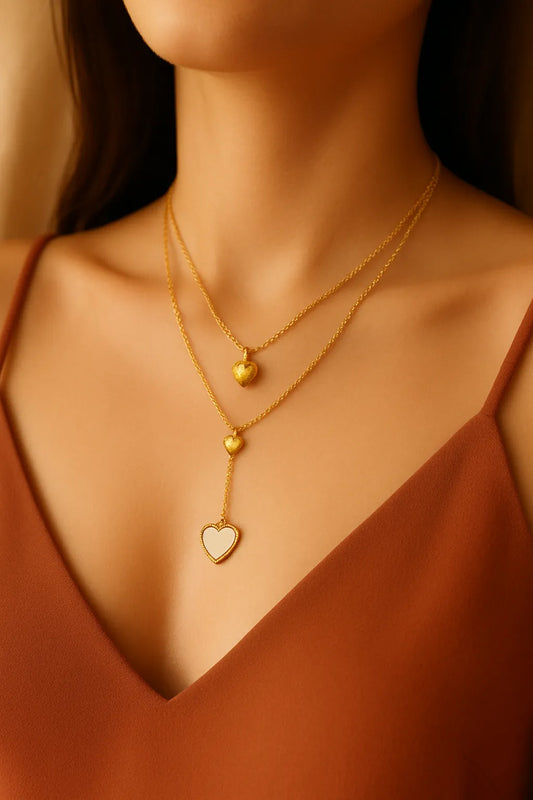 Gold necklace with heart pendant worn by a model against a neutral background