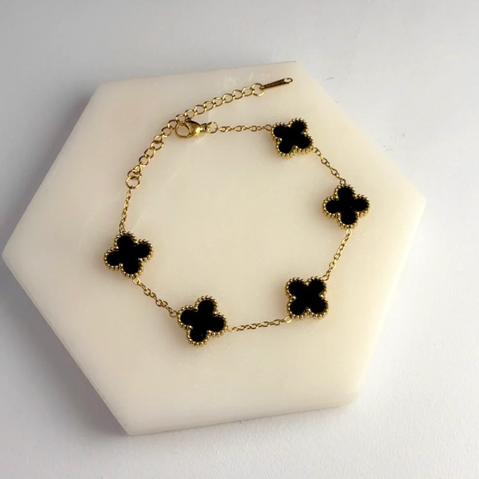 Gold bracelet with black clover-shaped charms on a white stand
