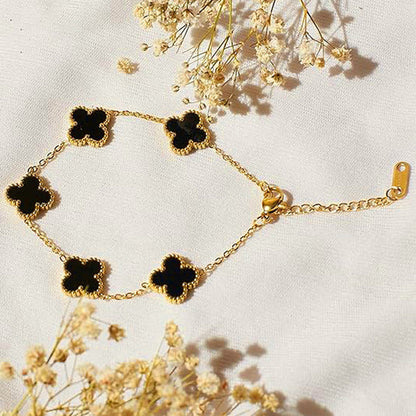 Gold bracelet with black clover-shaped charms on a light background with dried flowers.