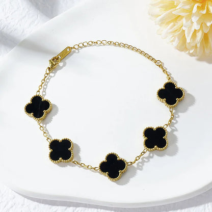 Gold necklace with black clover-shaped pendants on a white surface with a yellow flower.
