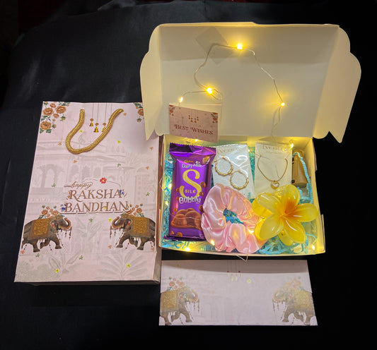 Gift box with Raksha Bandhan-themed items including a card, chocolate, and decorative items on a dark background.