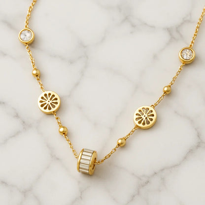 Gold-toned necklace featuring lotus-inspired medallions, bezel-set crystals, and a center baguette charm on adjustable chain.

