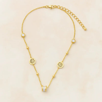 Gold-toned necklace featuring lotus-inspired medallions, bezel-set crystals, and a center baguette charm on adjustable chain.

