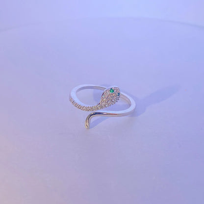 Silver snake-shaped ring with a green gemstone on a light purple background