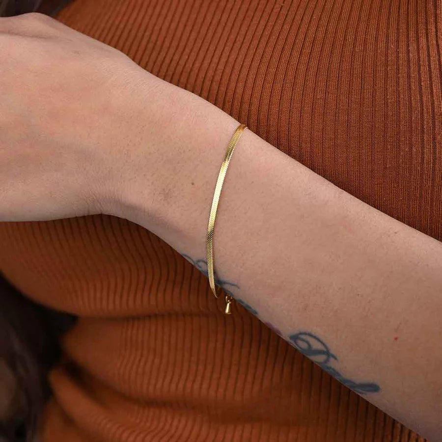 Gold Snake Chain bracelet  by everrayon a wrist against an orange textured background